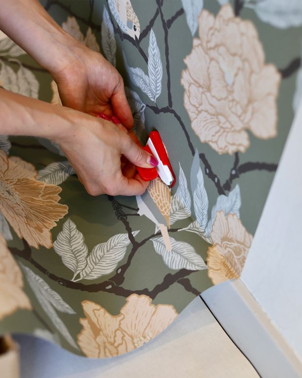 tapetsera och sk&auml;r av tapet med rakblad vid golvlist